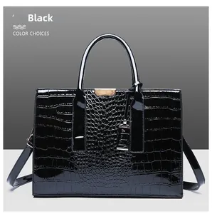 Detail of glossy black crocodile embossed handbag with gold hardware and strap