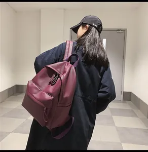 Burgundy faux leather backpack detail showing front zipper pocket and pebbled texture on model