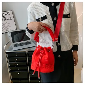 Detail of red plush bucket bag with The Bucket embossing and wide fabric strap