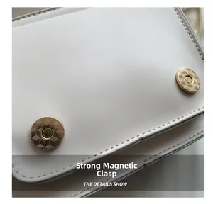 Detail van sterke gouden magneetsluitingen op een witte leren crossbody tas
