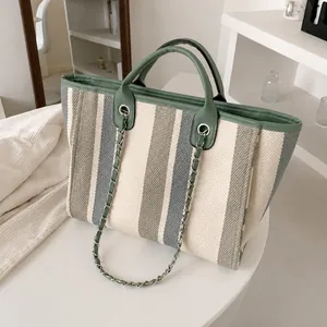 Detail of canvas tote bag with sage green stripes, leather handles and metal chain strap