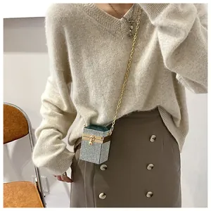 Vue détaillée du mini sac boîte en strass avec chaîne dorée sur un pull avoine