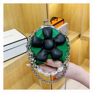 Detail of green mini bag featuring black leather flower, pearl handle and metal chain