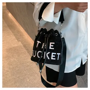 Detail of black velvet bucket bag featuring white THE BUCKET embroidery and wide strap
