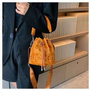 Detail showing ginger yellow suede bucket bag with THE BUCKET embossed text and strap