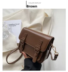 Detailopname van een bruine PU-lederen crossbodytas met dubbele decoratieve gespbanden