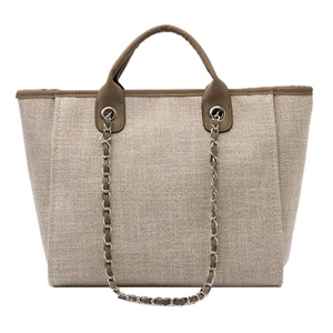 Detalle del bolso tote de lona beige con asas de cuero marrón y correa de cadena tejida