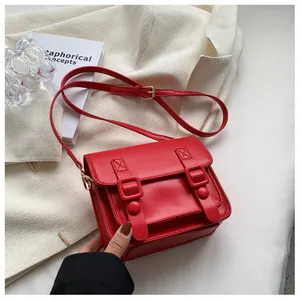 Detail van rode vintage crossbodytas met decoratieve dubbele gespen en gladde lederen textuur