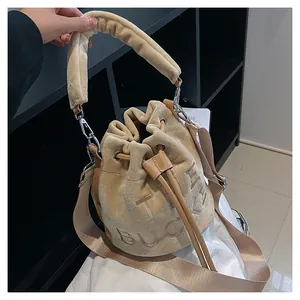 Detailed view of beige plush bucket bag with embossed The Bucket lettering and fuzzy handle