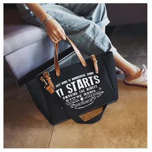 Detail der schwarzen Canvas-Tasche mit braunen Ledergriffen und weißem Grafikdruck