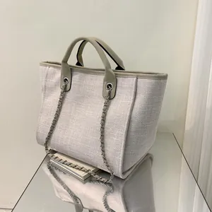 Detalle del bolso tote de lona con textura tejida, ribete de cuero y cadena de metal