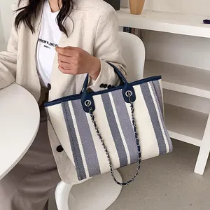 Grande borsa tote in tela a righe blu con manici in pelle e tracolla a catena su modella