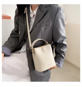 Close-up of cream-colored bucket bag with gold hardware and adjustable strap on a model