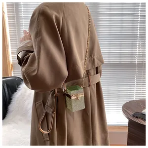 Détail d'un mini sac strass vert avec chaîne dorée porté sur un trench-coat classique