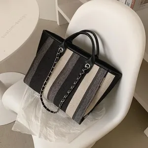 Borsa tote in tela a righe con tracolla a catena e manici in pelle su una sedia