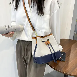 Canvas bucket bag with contrast leather trim, featuring a drawstring closure and shoulder strap