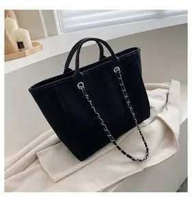 Detalle de bolso tote de lona negra con asas de cuero y correa de cadena de metal chic