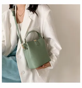 Close-up of light green bucket bag with gold hardware worn with a white blazer