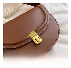 Close-up of a brown leather saddle bag featuring a textured gold metal twist-lock clasp