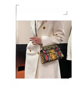 Detail of color-block snakeskin crossbody bag with metal clasp and woven strap