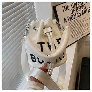Detail view of white plush bucket bag featuring black THE BUCKET text and wide shoulder strap