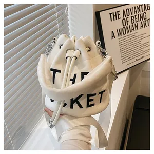 Detail of white plush bucket bag with THE BUCKET text and wide shoulder strap
