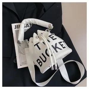 Detail of white plush bucket bag featuring black THE BUCKET text and wide shoulder strap