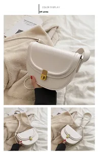 Detail of off-white PU leather saddle bag featuring a gold rotary lock and smooth texture