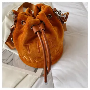 Close-up of orange velvet bucket bag with embroidered text and leather shoulder strap