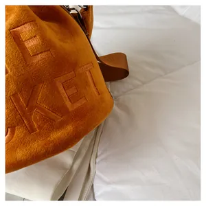 Detail view of orange plush bucket bag with KET embroidery and brown nylon strap