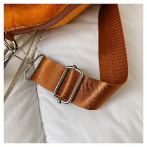 Close-up of orange velvet bag with brown nylon strap and shiny silver metal buckle