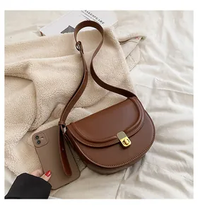 Close-up of brown PU leather saddle bag with gold metal buckle and a smartphone for scale