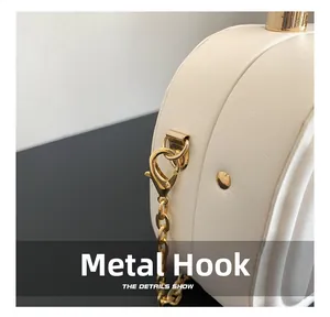 Détail du fermoir mousqueton doré et de la chaîne métallique sur un sac crème texturé