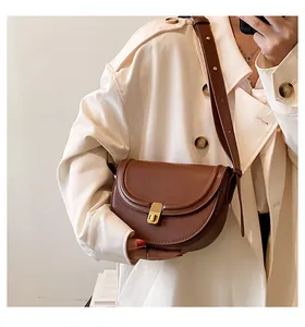 Brown PU leather saddle bag with gold clasp shown worn over a beige trench coat