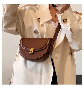 Close-up of a dark brown PU leather saddle bag with a golden clasp on a beige trench coat
