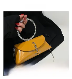 Close-up of mustard yellow handbag featuring a sparkling rhinestone ring handle and chain