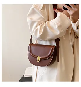 Brown PU leather saddle bag with gold buckle styled on a beige trench coat