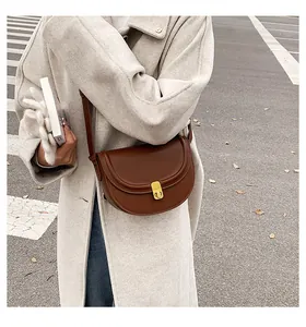 Detail of a brown leather saddle bag with gold buckle on a model wearing a beige coat