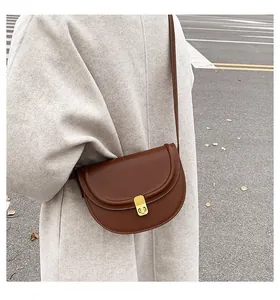 Deep brown saddle bag with gold buckle worn on a beige wool coat for fall style