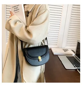 Close-up of black PU leather saddle bag with golden buckle on a wooden desk