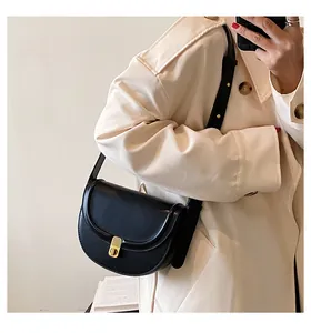 Close-up of black PU leather saddle bag with gold buckle on a beige trench coat