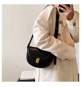 Fashionable black PU saddle bag with gold metal buckle styled on a beige trench coat
