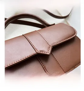 Detail view of brown faux leather handbag showing precise stitching and pointed flap design
