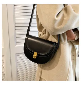 Close-up of a black PU leather saddle bag featuring a gold metal lock on a beige coat