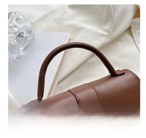 Detail of the cylindrical brown leather handle and stitching on a stylish handbag