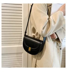 Detail of a black PU saddle bag with gold metal lock on a model in beige coat