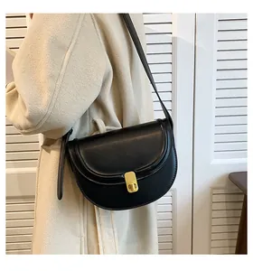 Detail of a black leather saddle bag with gold metal clasp on a beige wool coat