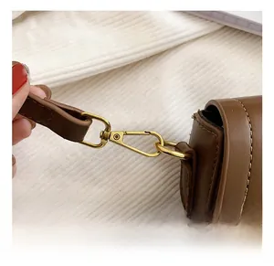 Detailed close-up of golden metal spring hook on brown leather shoulder bag strap