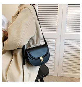 Close-up of black PU leather saddle bag with gold metal clasp on beige wool coat