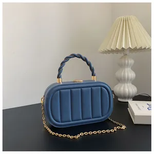 Détail du sac boîte bleu foncé avec gaufrage vertical et poignée torsadée dorée